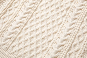 Dettaglio ravvicinato della trama a maglia a trecce su un maglione girocollo bianco