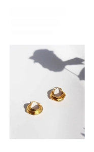 Macro shot of gold-plated thick C-hoop earrings with irregular hammered texture detail