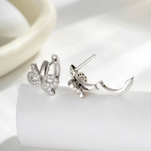 Elegant silver bow earrings with zircon stones and white ceramic on a white display pedestal