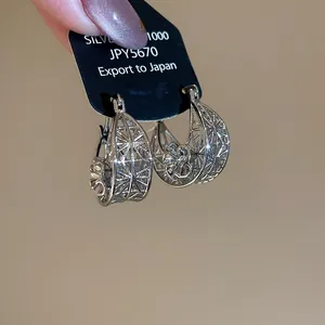 Macro shot of silver hollow-out flower pattern earrings with a Silver 1000 material tag