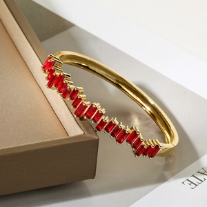 Dettaglio di un bracciale dorato con zirconi rossi rettangolari su una scatola da regalo