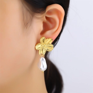 Detail of gold floral earring with irregular white pearl pendant on model ear
