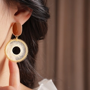Detail of woven grid pattern on a gold circle earring worn by a model in soft lighting