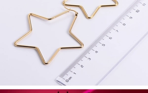 Detailansicht großer goldener Stern-Ohrringe neben einem Lineal zur Größenangabe