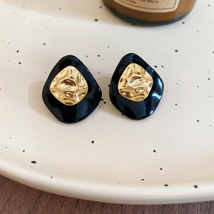 Detailed close-up of retro black and gold shield-shaped earrings on a textured tray