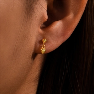 Close-up of heart-shaped gold stud earring worn on ear showing elegant metallic finish