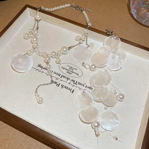 Detail view of elegant pearl necklace and shell earrings set on a wooden jewelry tray