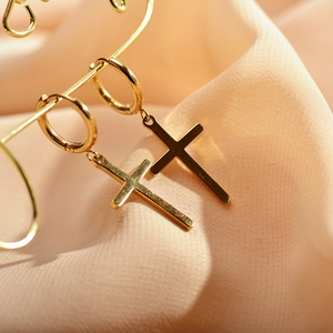 Detail of gold-plated hoop earrings featuring sleek cross pendants on textured fabric