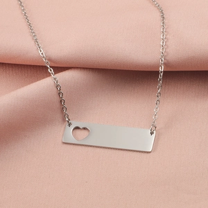 Detail of silver bar necklace featuring a hollow heart cutout on a pink silk background