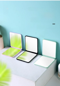 Three compact folding makeup mirrors in lavender, black, and mint green on a display stand