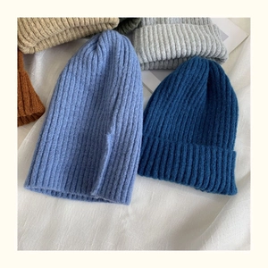 Detailed knit texture of assorted colorful winter beanies in a soft stack