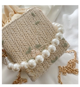Close-up of woven bag with flower embroidery, pearl handle, and gold chain strap