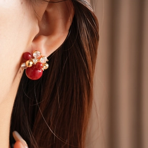 Close-up of gold-plated flower earrings with large red pearls and sparkling zircons
