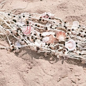 Detailed view of handwoven seashells and brown beads on a summer beach straw hat