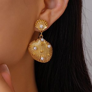 Detail of gold shell drop earrings with white pearls on model for holiday style