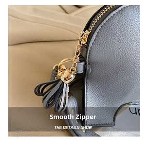 Detail of grey pebble leather bag showing smooth gold zipper, chain and tassel charm