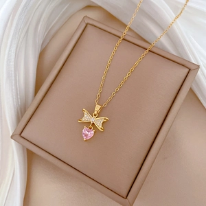 Gold butterfly bow necklace with pink heart gemstone on beige jewelry box with silk