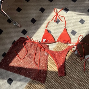 Flat lay of an orange three-piece bikini set with a crochet mesh skirt on a patterned rug