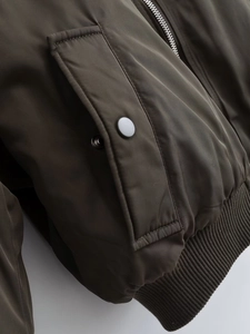 Detail of olive green bomber jacket with textured fabric, metal zipper, and ribbed hem