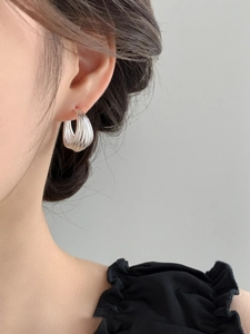Macro detail of textured silver multi-layer C-shaped hoop earrings on female model