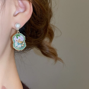 Detailed close-up of vintage enamel drop earrings with golden swan and pearl inlay