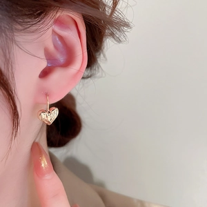 Close-up of gold-plated heart earrings with textured surface on female model