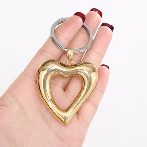 Detail of hand holding a large gold hollow heart keychain with polished metallic luster