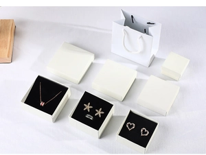 Detailed set of cream jewelry box, white gift bag, and accessories on white fabric