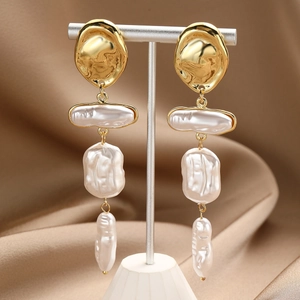 Detail view of long gold drop earrings with irregular white baroque pearls on T-stand