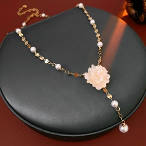 Detailed view of a gold flower necklace with white petals and pearls on a black display pad