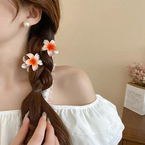 Detail of gradient orange and white flower hair claw clip worn by a model in soft light