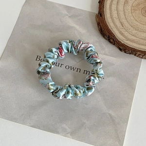 Detailed close-up of light blue floral satin scrunchie on a decorative wood slice