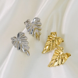 Leaf shaped stainless steel stud earrings in gold and silver finish on white silk background
