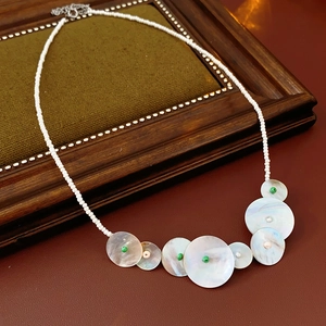 Detail of round shell necklace with green beads and extension chain on olive fabric