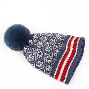 Detail of navy knit beanie with white snowflake pattern and large faux fur pom-pom