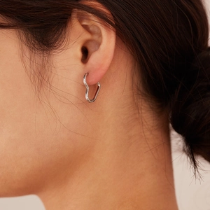 Minimalist silver heart-shaped stainless steel earrings worn by a model in a close-up view