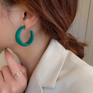 Close-up of a model wearing glossy green C-shaped hoop earrings and a gold heart ring