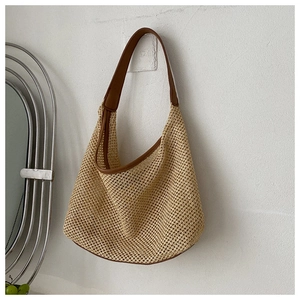 Detail of khaki woven hobo bag with brown leather shoulder strap on a white wall