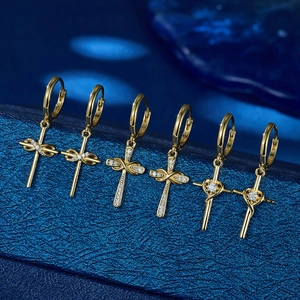 Detail view of gold cross hoop earrings with sparkling cubic zirconia on a blue surface