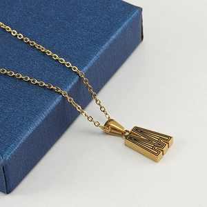 Golden stainless steel letter M pendant necklace on a blue jewelry box shown at a 45-degree angle