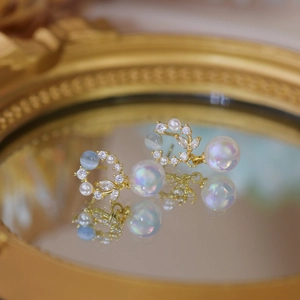 Macro detail of gold opal earrings featuring rainbow pearls and crystal flower accents