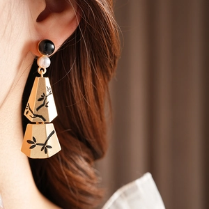 Detail of gold fringe earrings with black floral patterns and pearl beads on a model