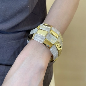 Close-up of wide checkerboard acrylic bangle with gold metal and white block details