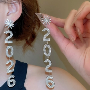 Détail de boucles d'oreilles fleuries scintillantes avec le chiffre 2026 et pompon long