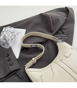 Detail der cremeweißen Handtasche aus Leder mit Lychee-Maserung und silbernen Nieten