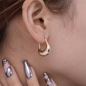 Detail of a minimalist gold-toned hollow geometric U-shaped earring worn on ear
