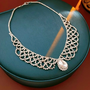 Macro shot of silver teardrop pendant necklace with clear rhinestone accents on a green box