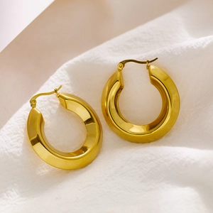 Macro shot of gold-plated stainless steel chunky hoop earrings on a white linen surface