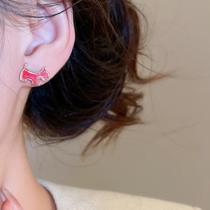 Close-up of red dog stud earrings with gold trim and glossy enamel finish on model