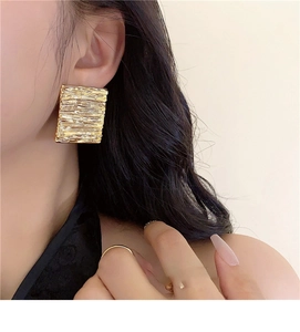 Detailed view of large gold square earrings featuring a unique ripple textured finish